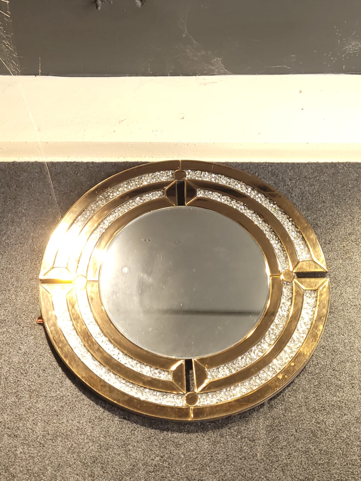 Round decorative mirror — A circular mirror framed by gold-toned and sparkling details.